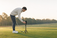 Golfer setting a phone on a low tripod at hip height beside the ball — the CaddieInsight capture setup
