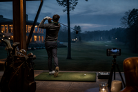 Evening practice session under clubhouse lights, phone filming from a tripod — the habit CaddieInsight is built around
